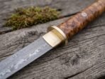 Close up of a Damascus katana blade with brass collar and guard below an olive burl wood handle with mosaic pin