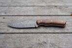 Damascus skinner knife with walnut wood handle laid flat in full profile on grey weathered wooden boards