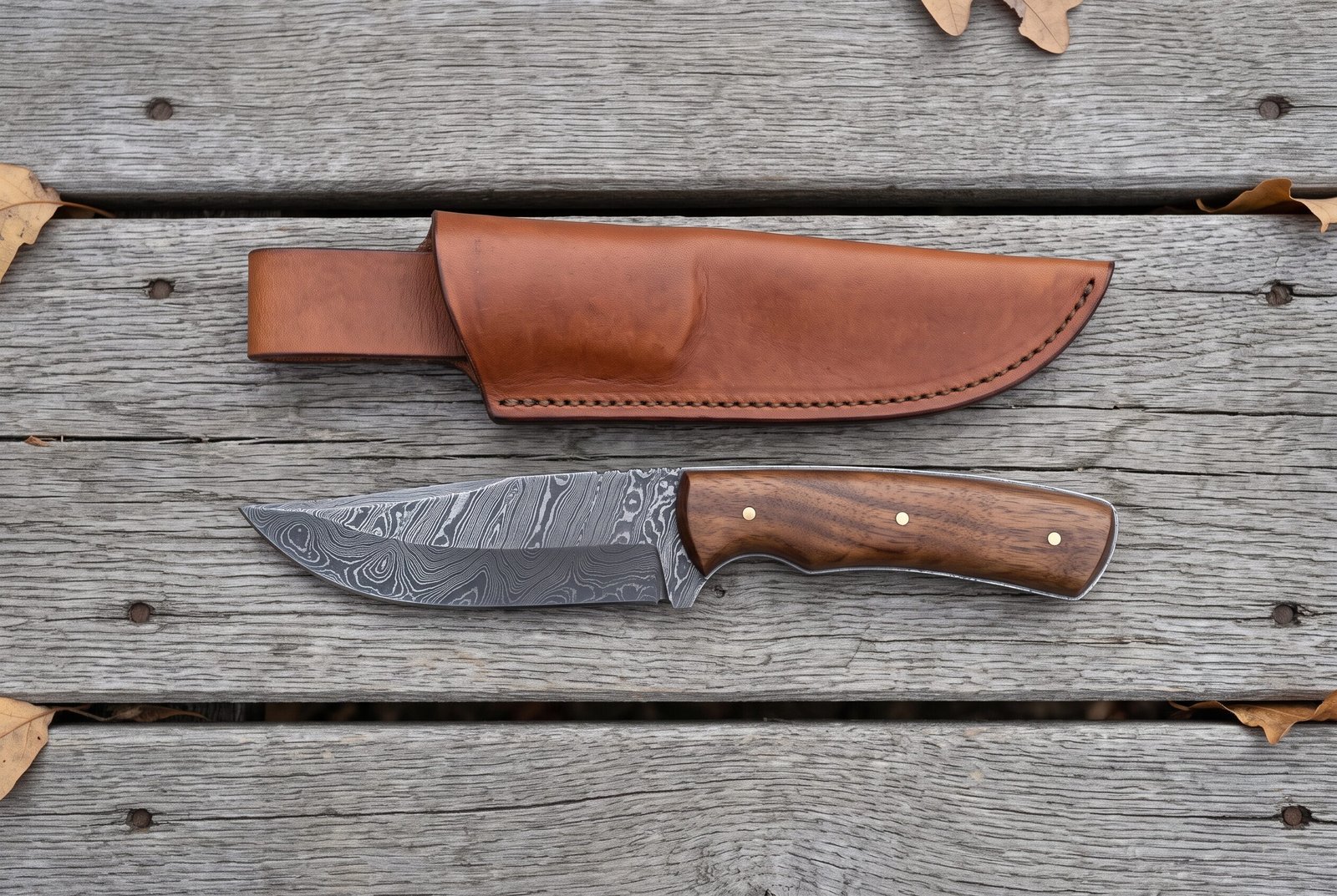 Overhead view of the Damascus skinner with walnut handle lying below its tan leather sheath on wooden boards Overhead view of the Damascus skinner with walnut handle lying below its tan leather sheath on wooden boards