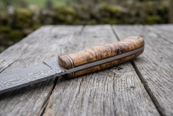 Stabilized wood handle of a Damascus skinner knife in close view, showing the fiber and brass spacers at the bolster