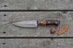 Damascus skinner knife with walnut and dark pakka wood handle lying on grey boards beside an acorn and oak leaf