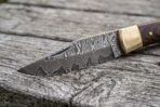 Damascus steel folding pocket knife blade in close view with brass bolster, open on weathered wood