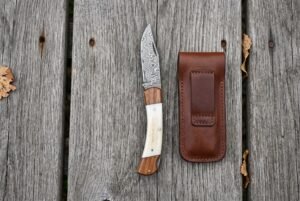 Overhead view of the open Damascus knife with bone and wood handle beside its brown leather belt pouch