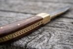 Pakka wood handle of a Damascus folding pocket knife in close view, brass bolster and decorated brass backspring