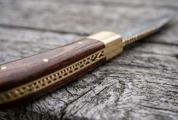 Pakka wood handle of a Damascus folding pocket knife in close view, brass bolster and decorated brass backspring