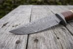 Damascus steel bowie knife blade in close view showing the swirling pattern and bolster on weathered planks