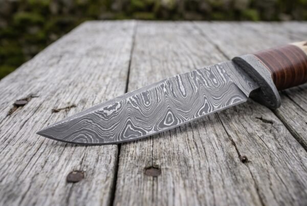 Damascus steel bowie knife blade in close view showing the swirling pattern and bolster on weathered planks