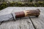 Stag horn and stacked leather bowie knife handle in close view with Damascus bolster, resting on old wood