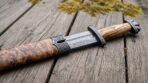 Damascus steel Viking sword with olive wood grip and lobed steel pommel lying on its olive burl scabbard on weathered planks