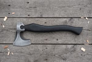 Bearded axe with a brushed steel head and curved black wood handle laid flat on grey weathered planks with wood chips