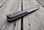 Close view of the black micarta handle, steel bolster and decorated spine of the Damascus skinner knife on grey wood