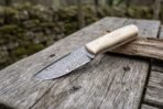 Camel bone handled Damascus knife resting on a wood block, blade pattern visible in side view on a plank table