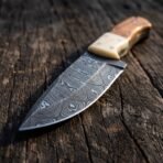 Close up of a Damascus skinner blade with camel bone bolster and wood handle resting on weathered wood
