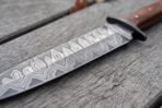 Close up of a Damascus steel dagger blade with wavy pattern, black guard and reddish wood handle on weathered grey planks