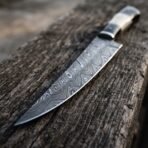 Close view of a Damascus steel fillet knife blade showing the flowing pattern, resting on a weathered wooden beam