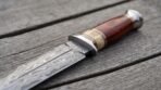 Close up of a Damascus dagger handle in wood and natural bone with brass spacers and polished steel bolster and pommel