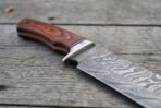Damascus bowie knife with rosewood handle and steel bolster in close view, blade pattern and handle joint in focus