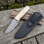 Damascus bull cutter knife with camel bone handle placed beside its black leather sheath on weathered boards