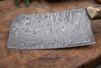 Damascus cleaver blade in close view on an end grain board, bold wave pattern across the wide flat face