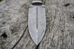 Damascus dagger blade from above in close view, central ridge and swirling steel pattern on grey weathered wood