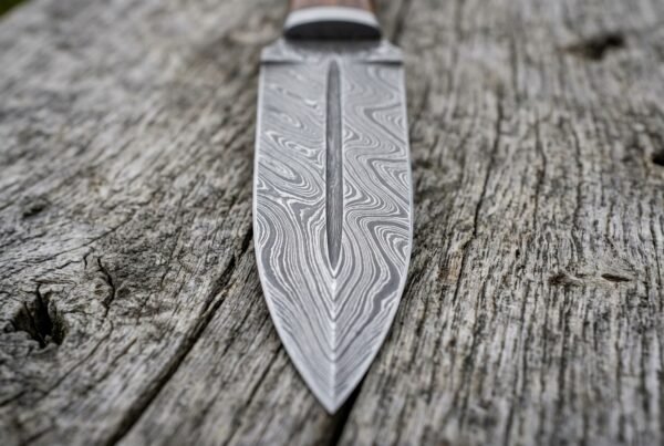 Damascus dagger blade from above in close view, central ridge and swirling steel pattern on grey weathered wood