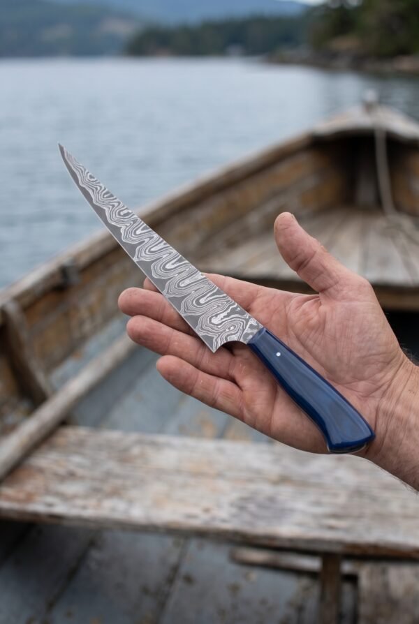 Damascus fillet knife with blue resin handle balanced on an open palm above an old wooden boat on the water