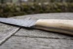 Damascus fish fillet knife with natural bone handle, close view of the bolster joint and handle on a weathered wooden table