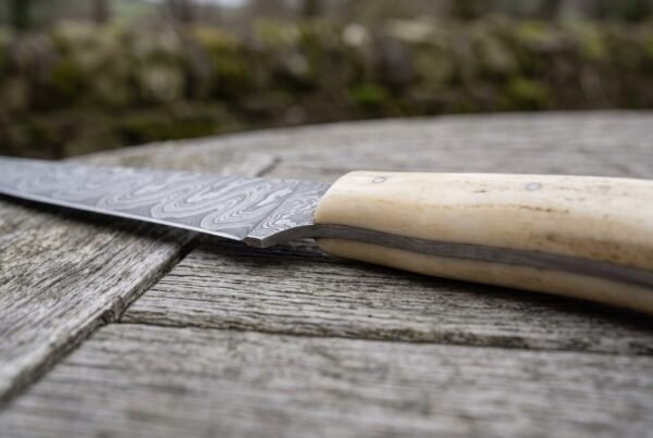Damascus fish fillet knife with natural bone handle, close view of the bolster joint and handle on a weathered wooden table