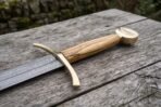 Damascus longsword grip in close view, olive wood handle with curved brass crossguard and round brass pommel on old planks