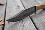 Damascus steel bowie knife blade in close view showing the wavy pattern along the edge on weathered boards