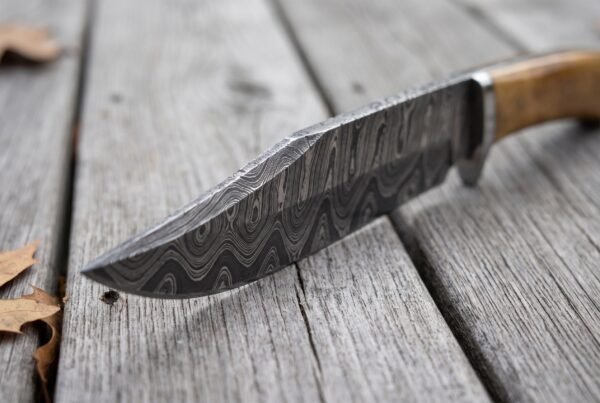 Damascus steel bowie knife blade in close view showing the wavy pattern along the edge on weathered boards
