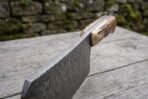 Damascus steel cleaver seen from the spine end, stag horn handle raised on a weathered wooden table