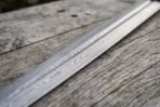 Damascus steel dagger sword blade in close view on old wood, layered pattern running along the fuller and edge