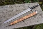 Damascus steel dagger sword with wrapped leather handle beside its olive burl wood scabbard on a weathered table