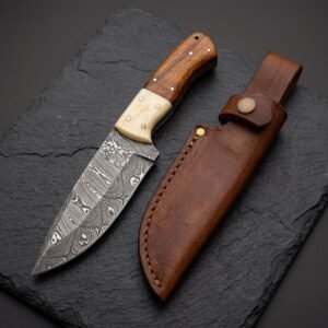Damascus steel skinner knife with camel bone and wood handle beside its brown leather sheath on dark slate