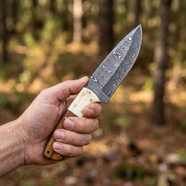 Hand holding a Damascus skinner knife with camel bone and wood handle against a blurred forest background