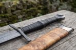Close view of the wrapped leather grip, crossguard and pommel of a Damascus dagger sword above its olive burl scabbard