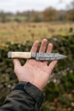 Damascus knife with camel bone handle and Damascus bolsters laid across an open hand in a green field