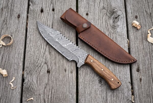 Overhead view of a Damascus tracker knife with hardwood handle beside its brown leather sheath and wood curls