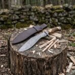 Damascus kukri knife with stag horn handle on a tree stump with its dark brown leather sheath and split kindling