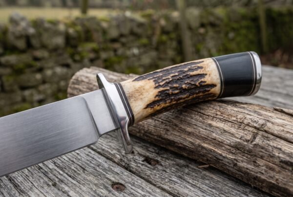 Bowie knife with stag horn and black micarta handle, close view of the steel guard and polished blade resting on a weathered log