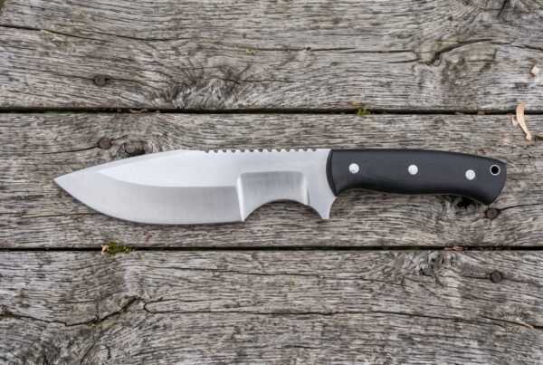 Hand forged tracker knife with black micarta handle shown in full side profile on grey weathered boards