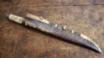 Bone handled seax in its tooled brown leather sheath with brass fittings and raven mounts on an old wooden table