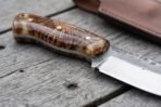 Close up of a stabilised pine cone resin knife handle with brass pins and a forge finished skinner blade on grey planks