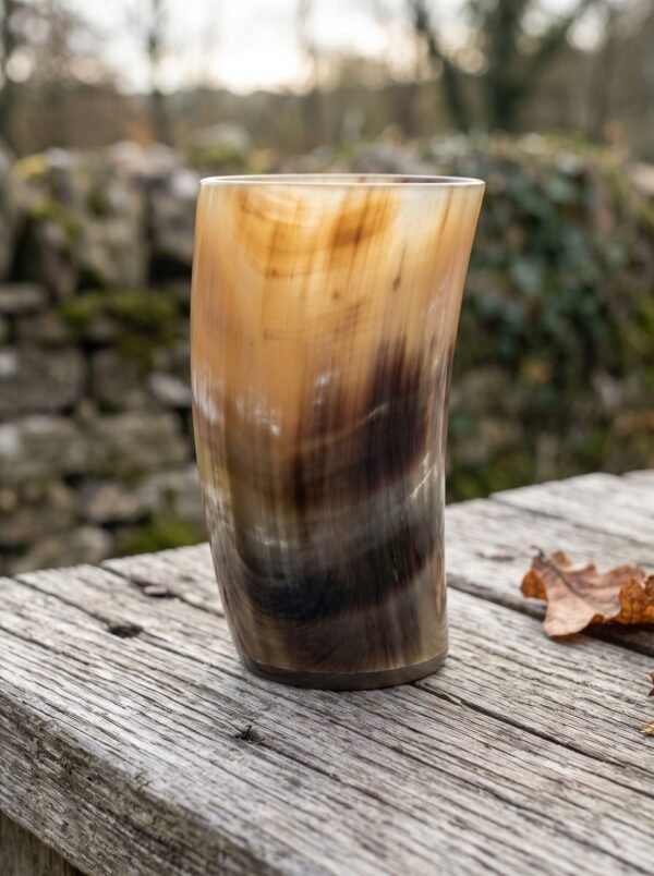 Natural horn beer mug with polished amber and dark banding standing upright on an old wooden rail by a mossy stone wall