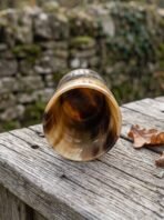 Polished natural horn beer mug lying on its side on a wooden rail, open mouth and inner horn grain in view