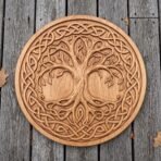 Round wooden Viking shield with carved tree of life and knotwork ring laid flat on grey decking with dry leaves