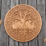 Round wooden Viking shield with carved tree of life and knotwork ring laid flat on grey decking with dry leaves