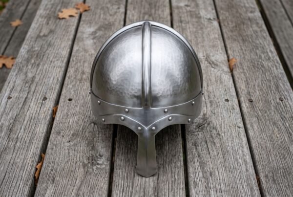 Steel Norse helmet with hammered skull and long nasal guard seen from the front on grey wooden decking with fallen leaves