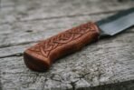 Viking seax knife close up of the engraved rosewood handle with carved knotwork pattern on a weathered plank